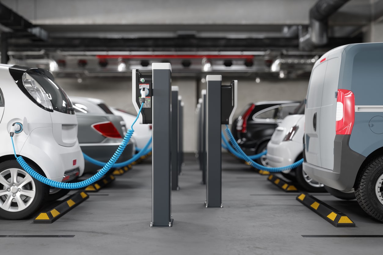 Electric vehicles charging at a parking station with blue cables connected to charging units.